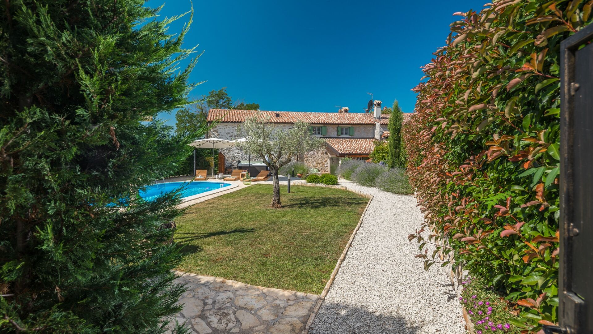 A villa with a swimming pool, stone pathway, and lush greenery.