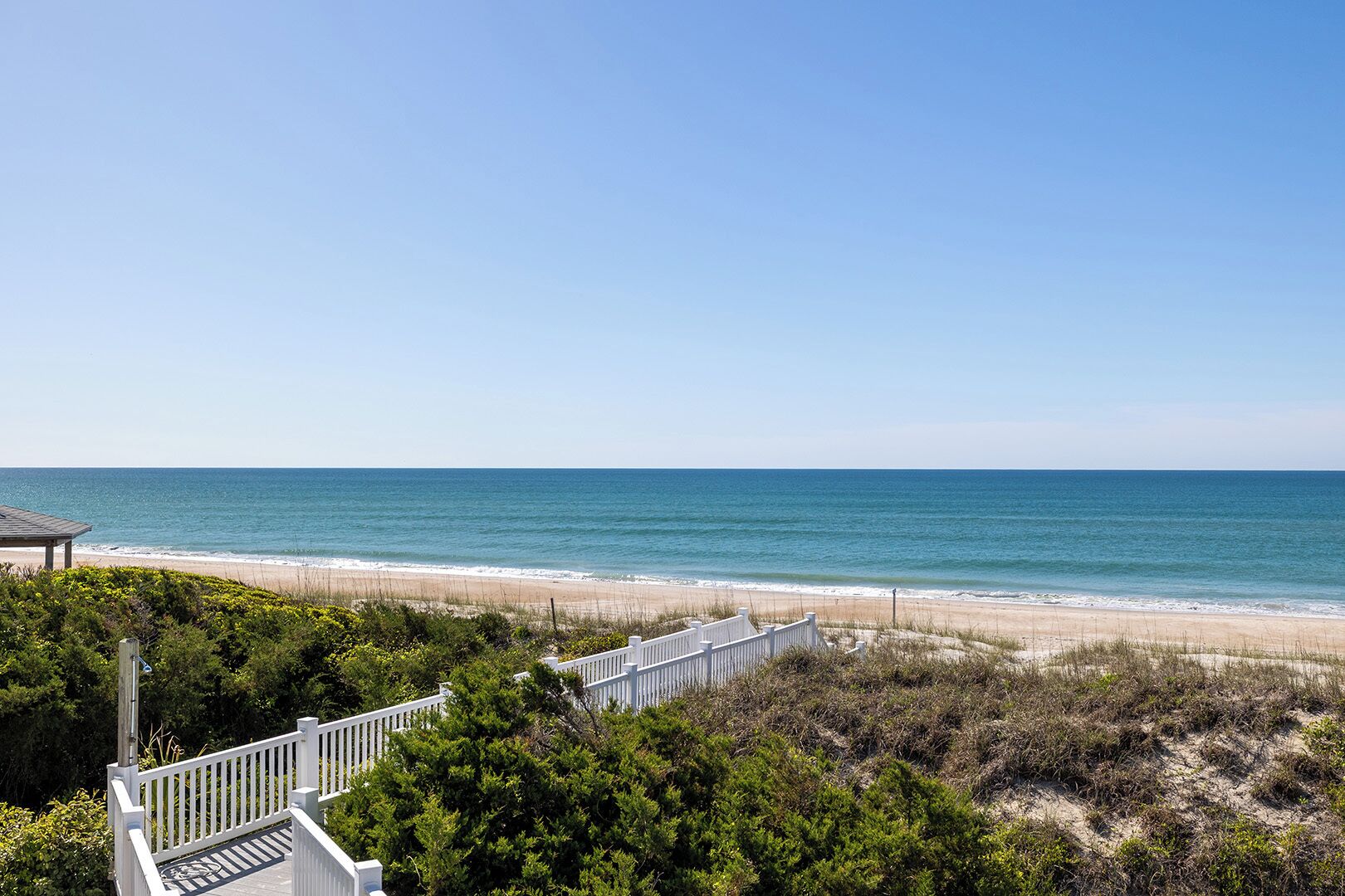 A beach view with a white fence and greenery in the foreground.
