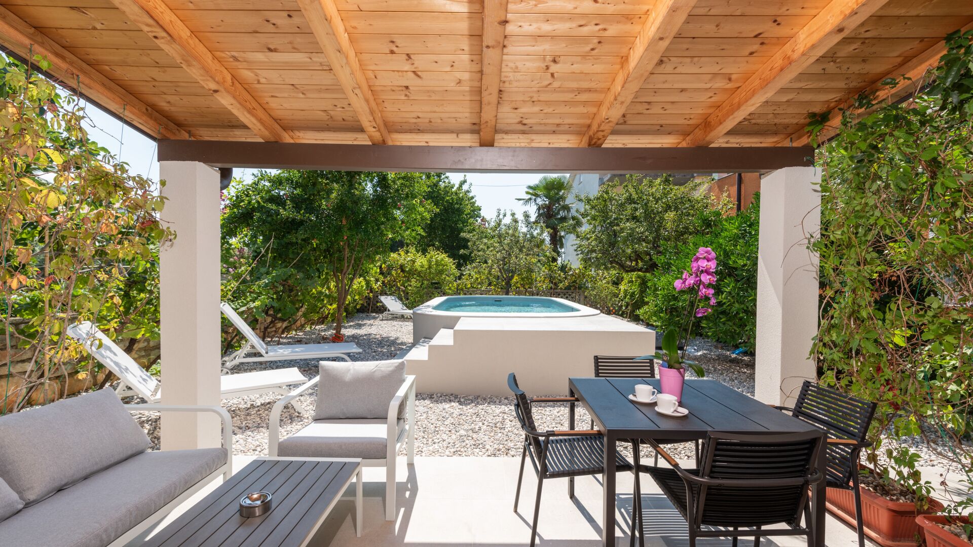 A covered outdoor area with a pool, seating, and greenery.