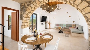 Uma área de jantar com um arco de pedra, uma TV na parede e um sofá ao fundo.