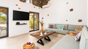 Ampla sala de estar com parede de pedra, televisão de tela plana, sofá e mesa de jantar com uma tigela de frutas.