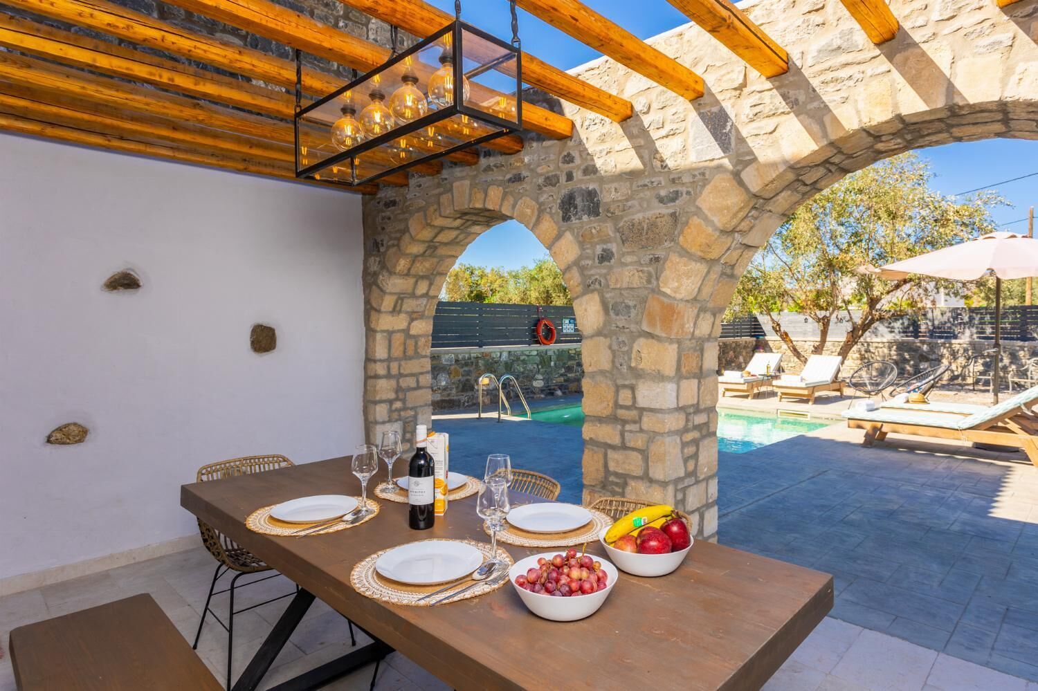 Un espacio exterior para comer con arcos de piedra, una piscina y sillones de descanso.