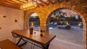 Uma área de refeições ao ar livre com arcos de pedra, piscina e espreguiçadeiras.