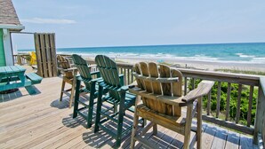 Een houten terras met groene Adirondack-stoelen en een picknicktafel met uitzicht op het strand.