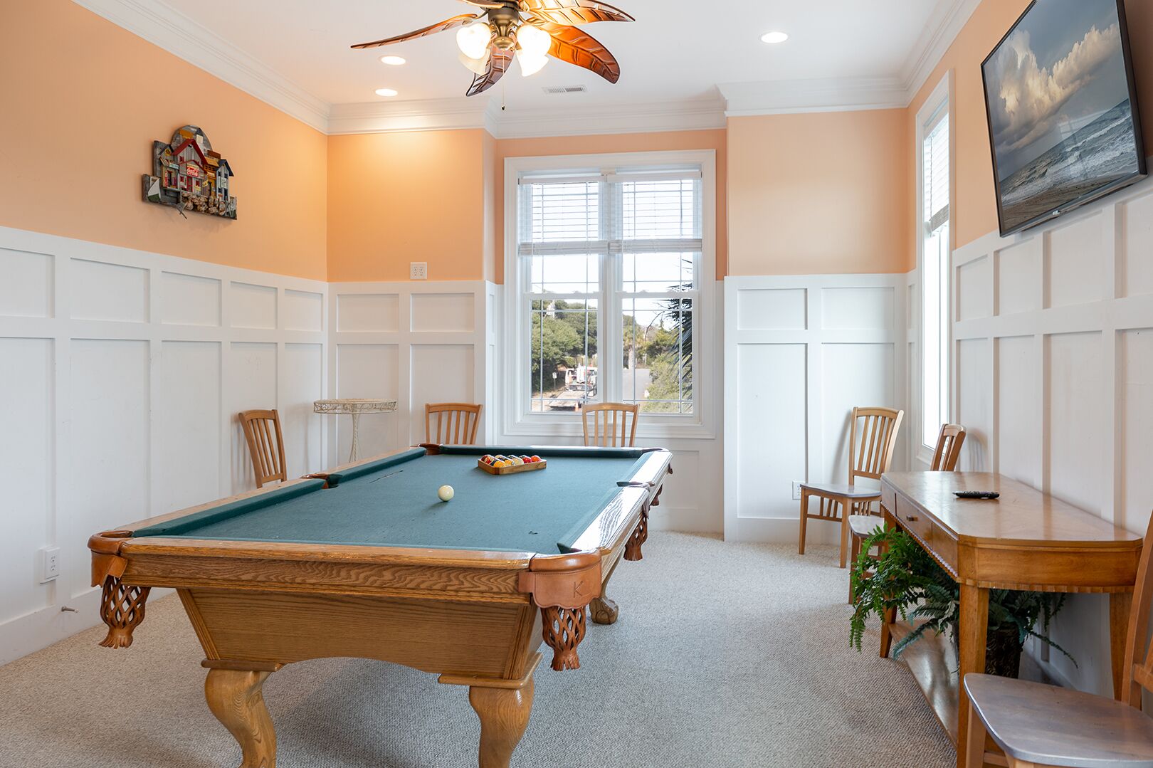 A pool room with a pool table, chairs, a television, and a window with a view.