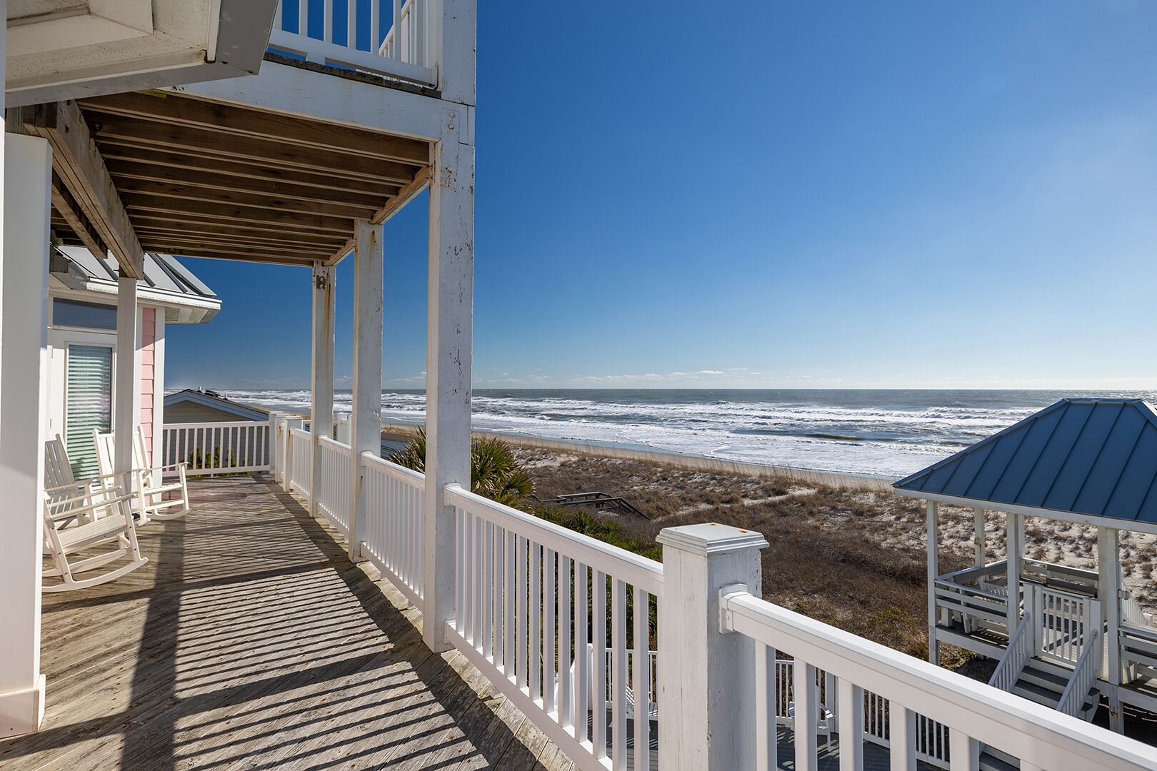 A wooden deck with white railings overlooking a beach.