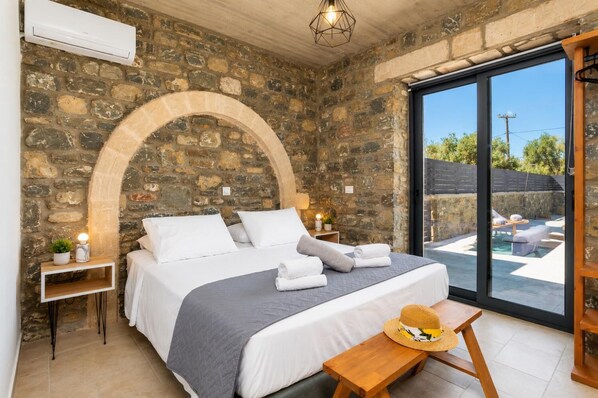 Ein Schlafzimmer mit Steinsandsteinwand, einem Bett mit weißer Bettwäsche, einer Bank, einem Hut und Blick auf einen Außenbereich.