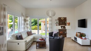A modern living room with a sofa, coffee table, and a black armchair. There is a TV mounted on the wall and a bookshelf with decorative items.