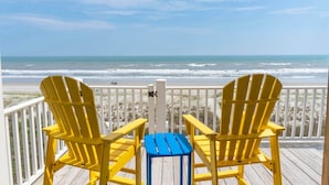 Due poltrone Adirondack gialle su un pontile di legno con vista su una spiaggia e onde.