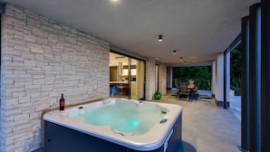Un área de spa moderna con una bañera de hidromasaje, pared de piedra y un comedor con vistas al verdor.