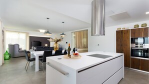 Una cocina moderna con una isla central, comedor con sillas y sala de estar con sofá y televisor.