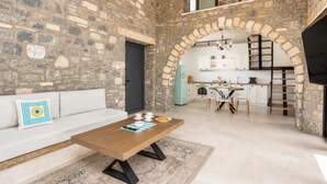 Un interior de paredes de piedra con un sofá, una mesa de centro, una zona de cocina y un espacio en alto.