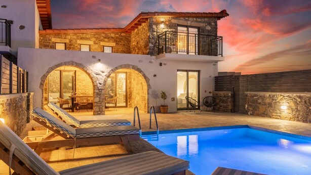 Un área junto a la piscina con sillones reclinables y un edificio de piedra con balcón.