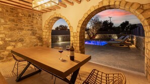 Un patio al aire libre con pared de piedra, piscina y una mesa con sillas.