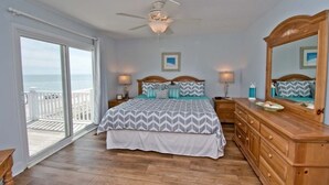 A bedroom with a bed, a dresser, a ceiling fan, and a view of the ocean through a sliding glass door. - Tides Out West, Oceanfront Duplex in Emerald Isle, NC! (Emerald Isle)