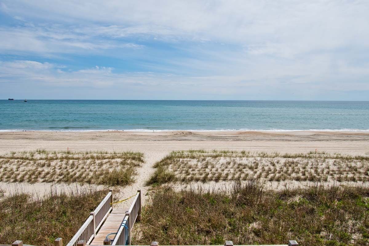 A beach with a wooden boardwalk leading to the shore, sandy dunes, and the ocean.