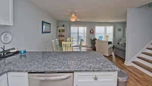 A kitchen with granite countertops, white cabinets, a ceiling fan, and a view to the outside. - Tides Out West, Oceanfront Duplex in Emerald Isle, NC! (Emerald Isle)