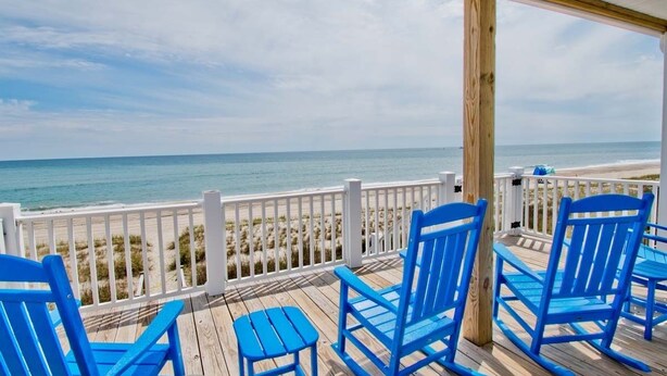 A wooden deck with blue chairs and a white railing overlooking a beach. - Tides Out West, Oceanfront Duplex in Emerald Isle, NC! (Emerald Isle)