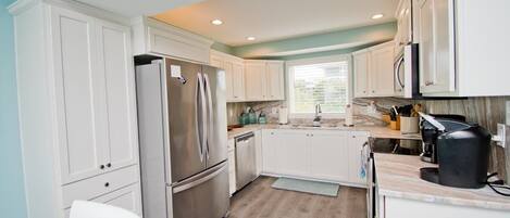 A modern kitchen with white cabinets, a stainless steel refrigerator, and a coffee maker.