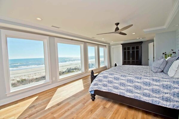 Une chambre avec un grand lit, de nombreuses fenêtres et une vue sur la plage.