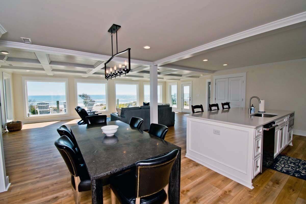 A spacious kitchen with a large island, dining area with a dark table and chairs, and a view of the ocean.