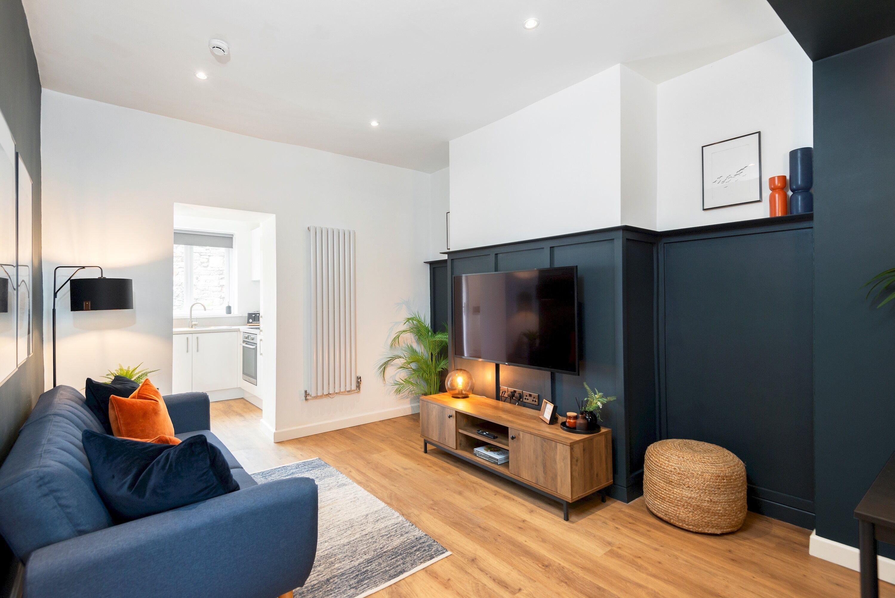 Una sala de estar moderna con una pared de acento oscura, un televisor de pantalla plana, un sofá azul y un mueble de entretenimiento de madera.