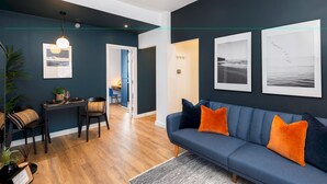 Una sala de estar moderna con un sofá azul oscuro, cojines anaranjados y cuadros enmarcados en la pared.