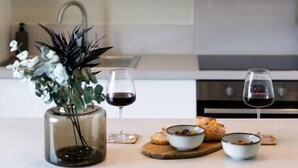 Une cuisine moderne avec des meubles blancs, un vase en verre contenant des fleurs et deux verres à vin posés sur le comptoir.