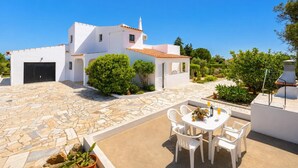 A white villa with a stone patio, a dining area with white chairs, and a small garden. - Casa Das Areias - Three Bedroom Villa, Sleeps 6 (Porches)