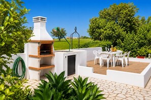 An outdoor patio with a brick oven, white chairs, and a table set for dining.