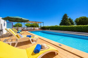 A poolside area with sun loungers, a covered seating area, and a clear view of the pool.