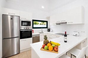 Une cuisine moderne dotée d’appareils électroménagers en acier inoxydable, d’un téléviseur à écran plat et d’un présentoir pour les fruits et les bouteilles de vin sur le comptoir.