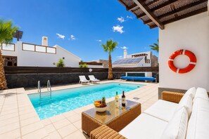 A pool area with lounge chairs, a table with bottles, and a life preserver on the wall.