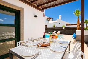 An outdoor dining area with a table set for two, a bottle of wine, and a bowl of fruit.