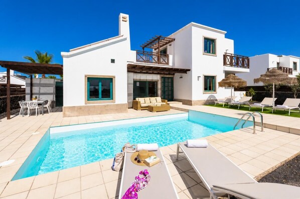 A modern two-story house with a swimming pool, outdoor seating, and a pergola.