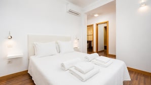 Hotelkamer met een groot bed, witte lakens, een nachtkastje, wandlampen en een houten vloer.