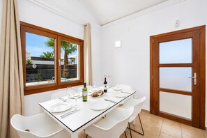 Un coin repas avec une table dressée pour quatre personnes, une bouteille de vin et une vue sur les palmiers à l’extérieur.