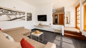 Uma sala de estar moderna com um sofá, uma mesa de centro, uma televisão e obras de arte na parede.