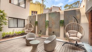 Patio moderno all'aperto con mobili in vimini, un pavimento in legno e un muro in pietra con vegetazione.