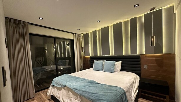 Una camera da letto moderna con un letto grande, una porta scorrevole in vetro che dà su un balcone e illuminazione a incasso nel soffitto.
