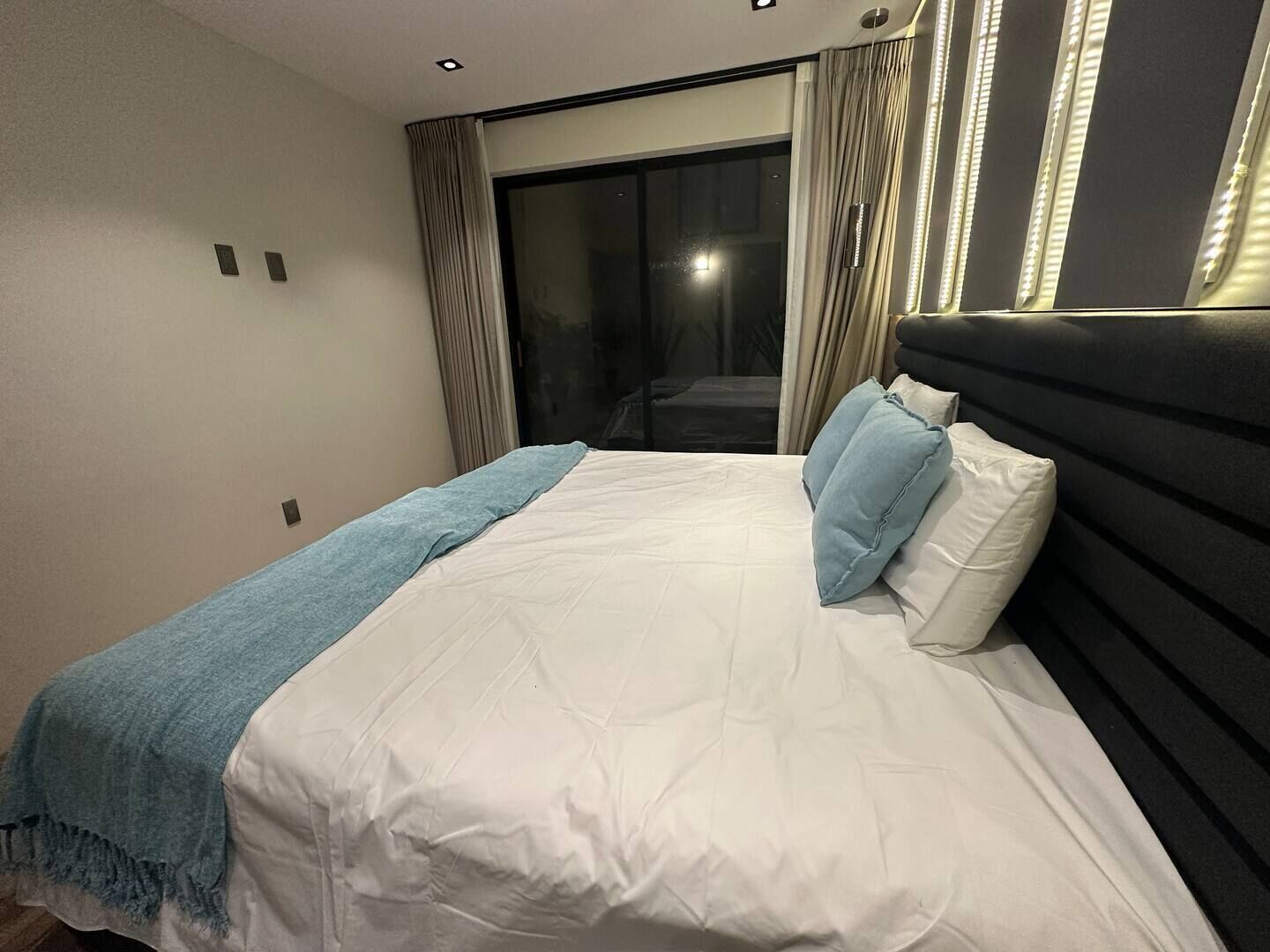A modern bedroom with a large bed, a blue throw blanket, and a view of a balcony.