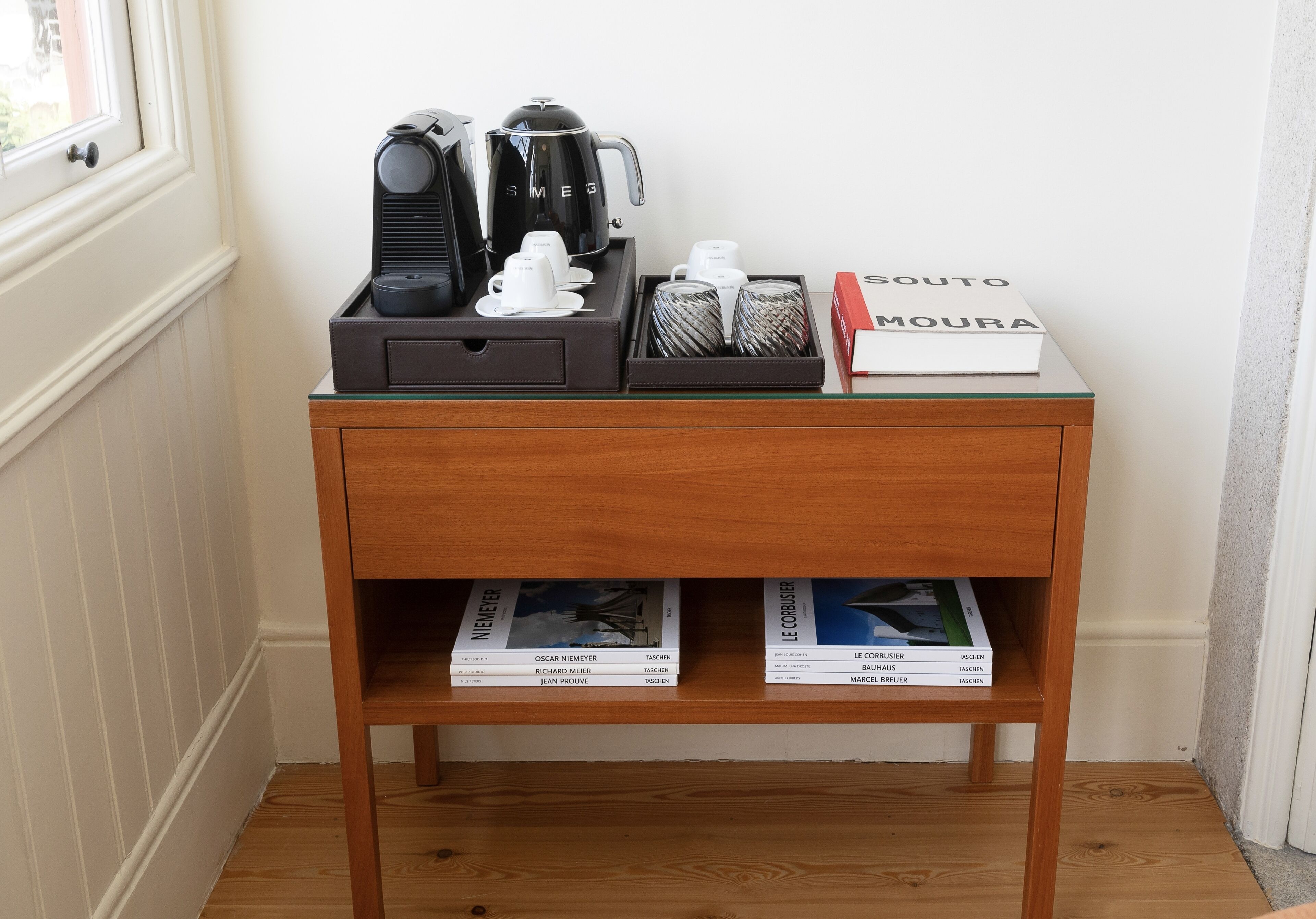 A wooden side table with a coffee maker, cups, and a book titled "SOUTO MOURA".