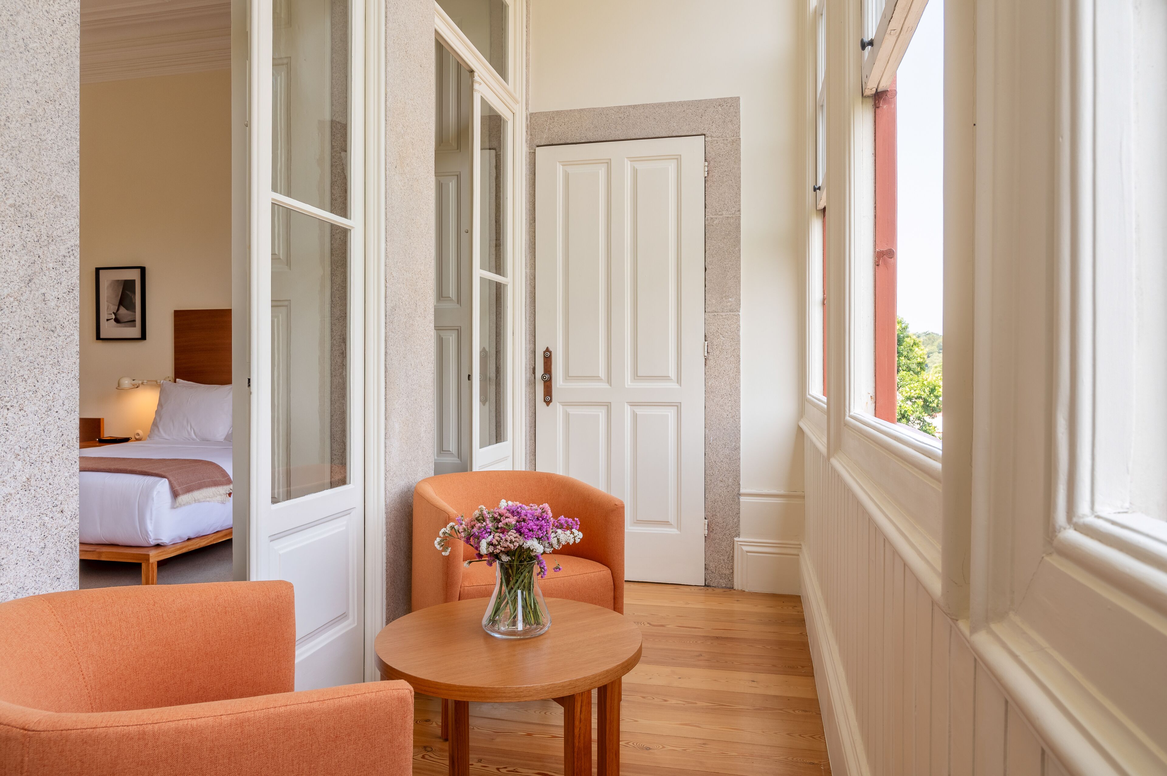 A narrow hallway with a wooden floor, a white door, and a small table with a vase of flowers.