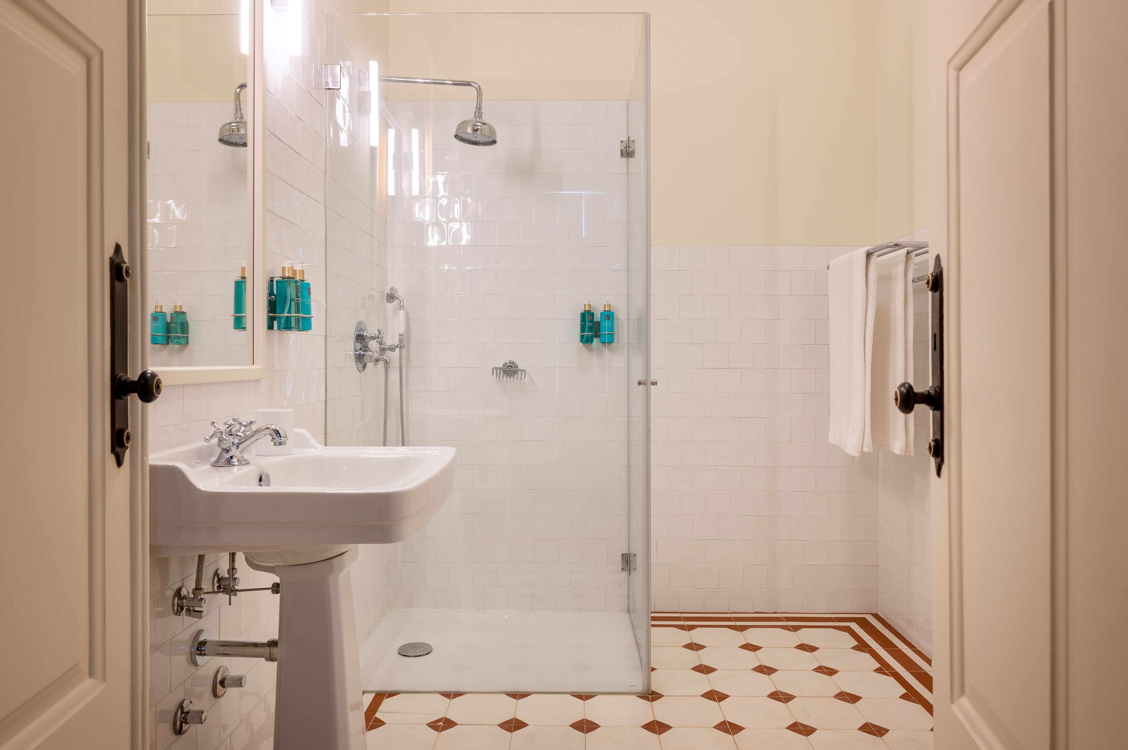 A bathroom with a white sink, a glass-enclosed shower, and a tiled floor with a diamond pattern.