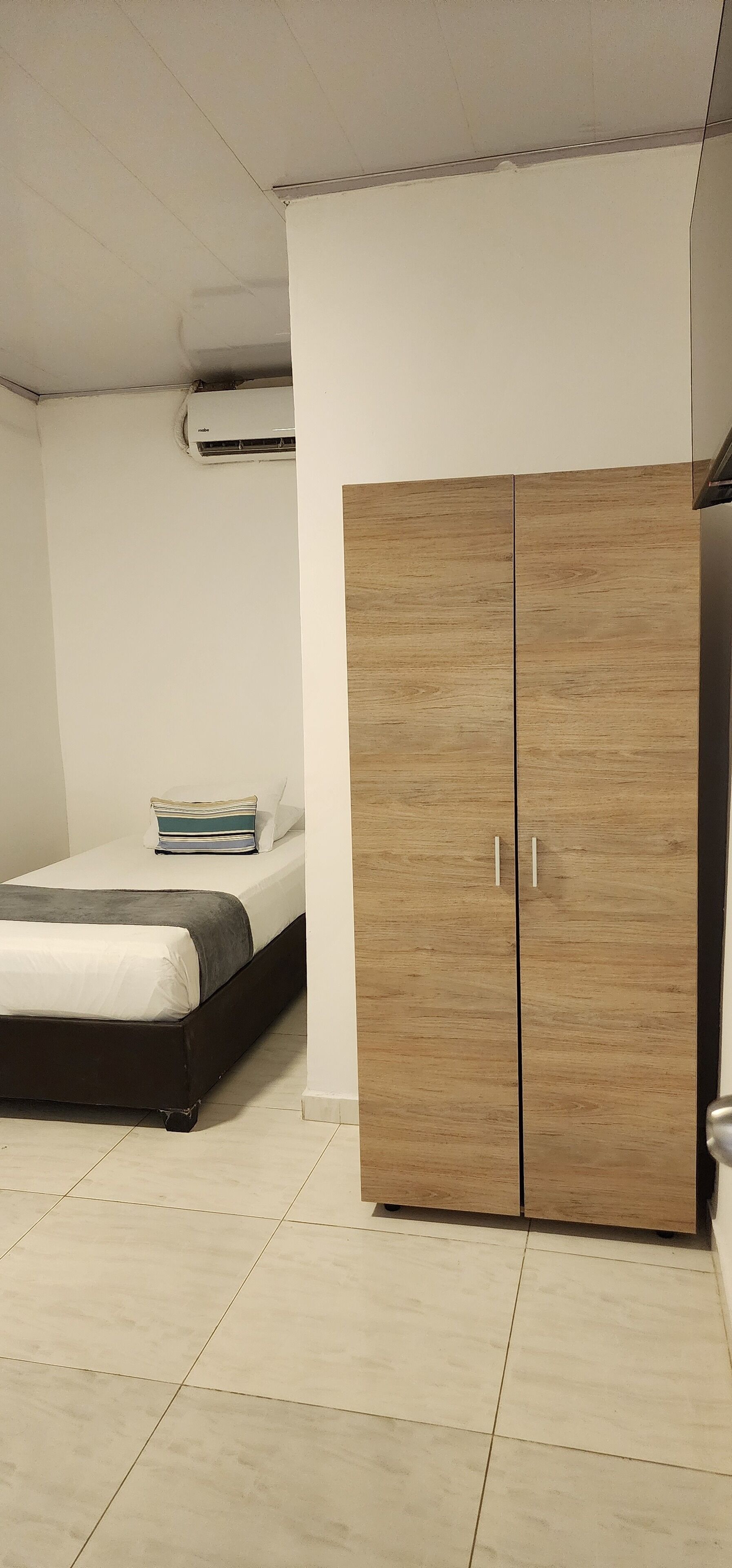 A bedroom with a bed, a wardrobe, and a ceiling-mounted air conditioning unit.