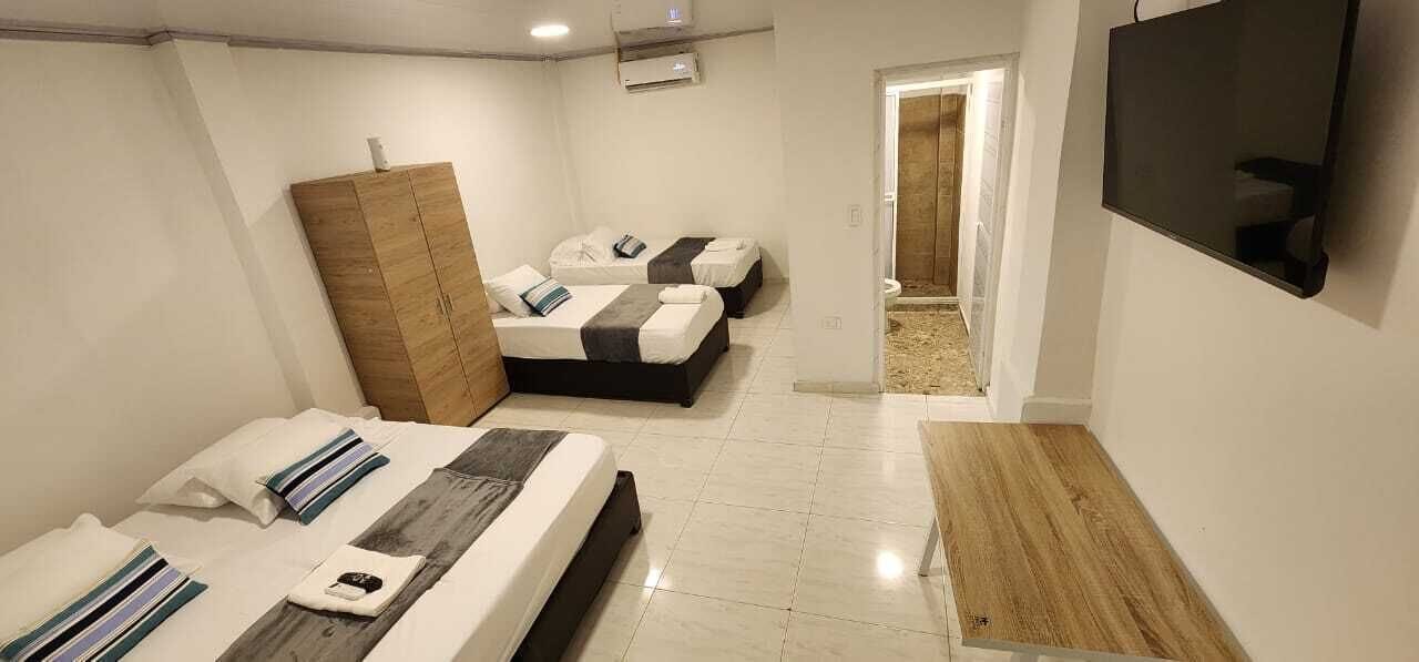 A hotel room with two beds, a wooden wardrobe, a TV, and a bathroom visible through an open door.