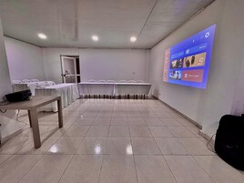 Un salón de conferencias con una larga mesa, sillas, una pantalla de proyector y un orador.