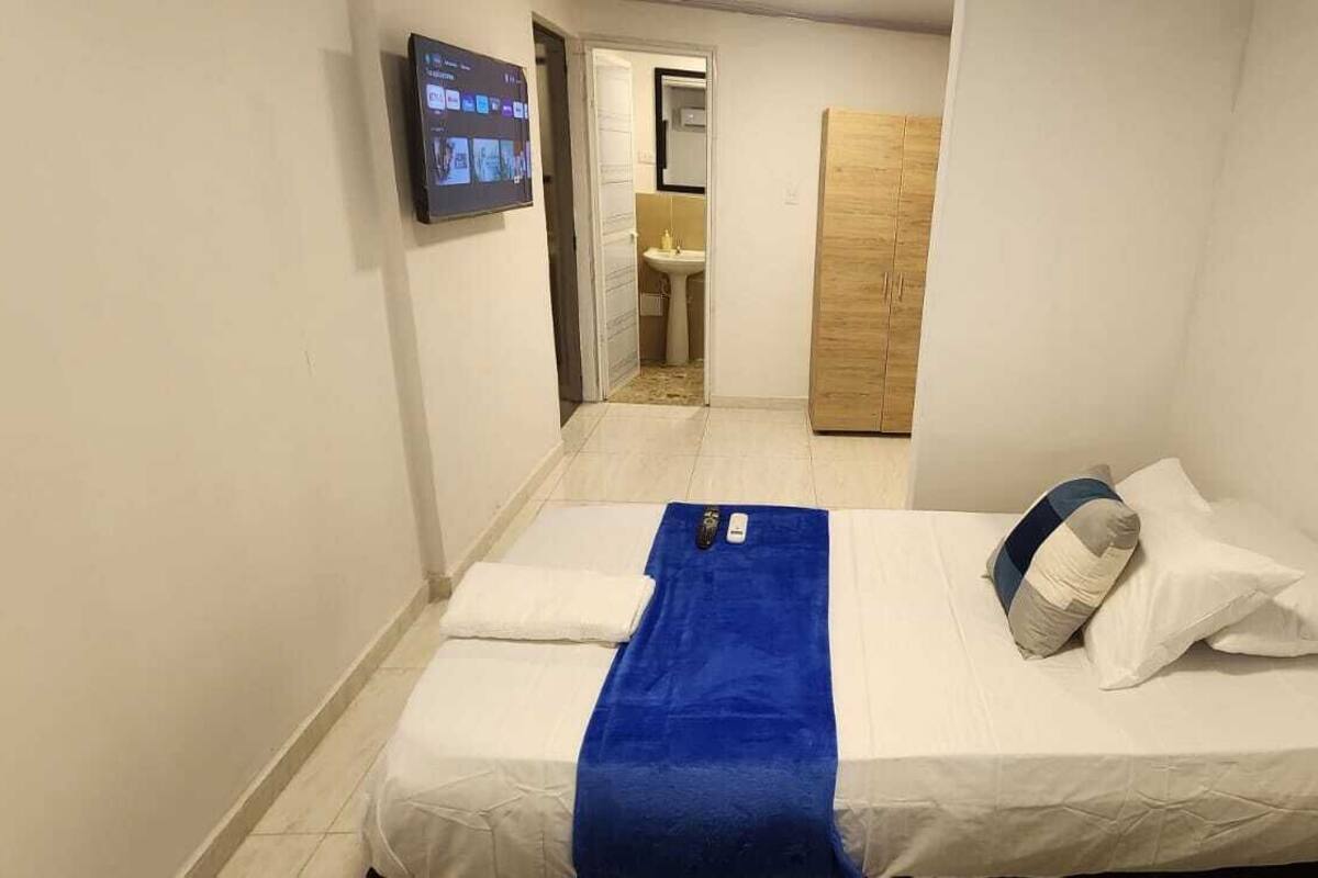Ein kleines, schmales Hotelzimmer mit einem Bett, einem blauen Handtuch und einem an der Wand montierten Fernseher.