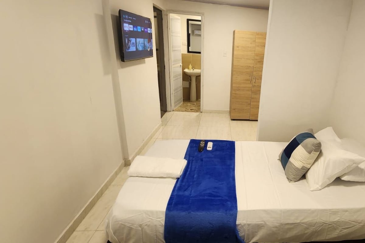 A narrow hotel room with a bed, a blue towel, and a TV on the wall.