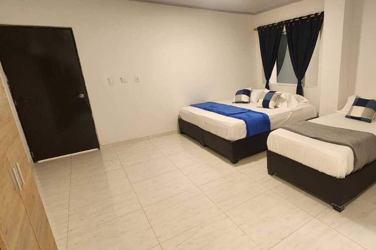 Ein Zimmer mit zwei Betten, einer Tür und einem mit Vorhängen versehenen Fenster.